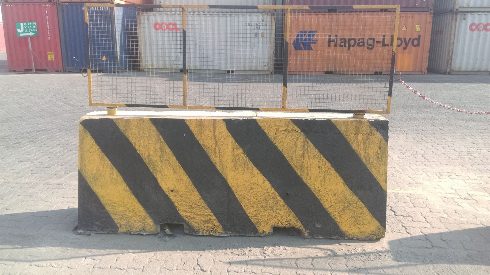 Precast concrete barrier with mesh fencing and yellow-black markings at a container terminal